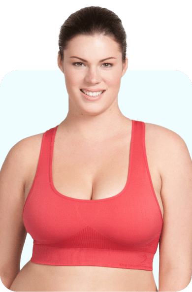 A woman with dark hair wearing a red sports bra is smiling and looking at the camera. She has a light-colored background.